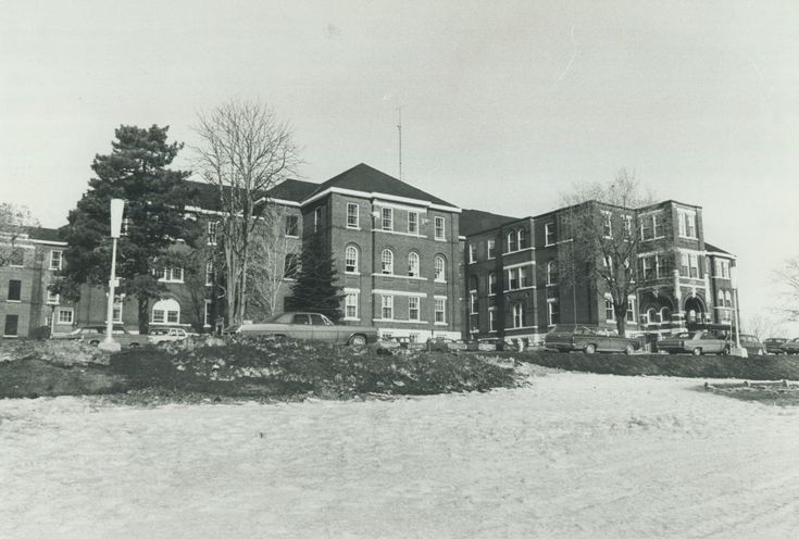 A black and white photograph of Huronia Regional Centre, circa the 1970s. It is a large, imposing brick building on a grassy hill with a few trees scattered around it. 